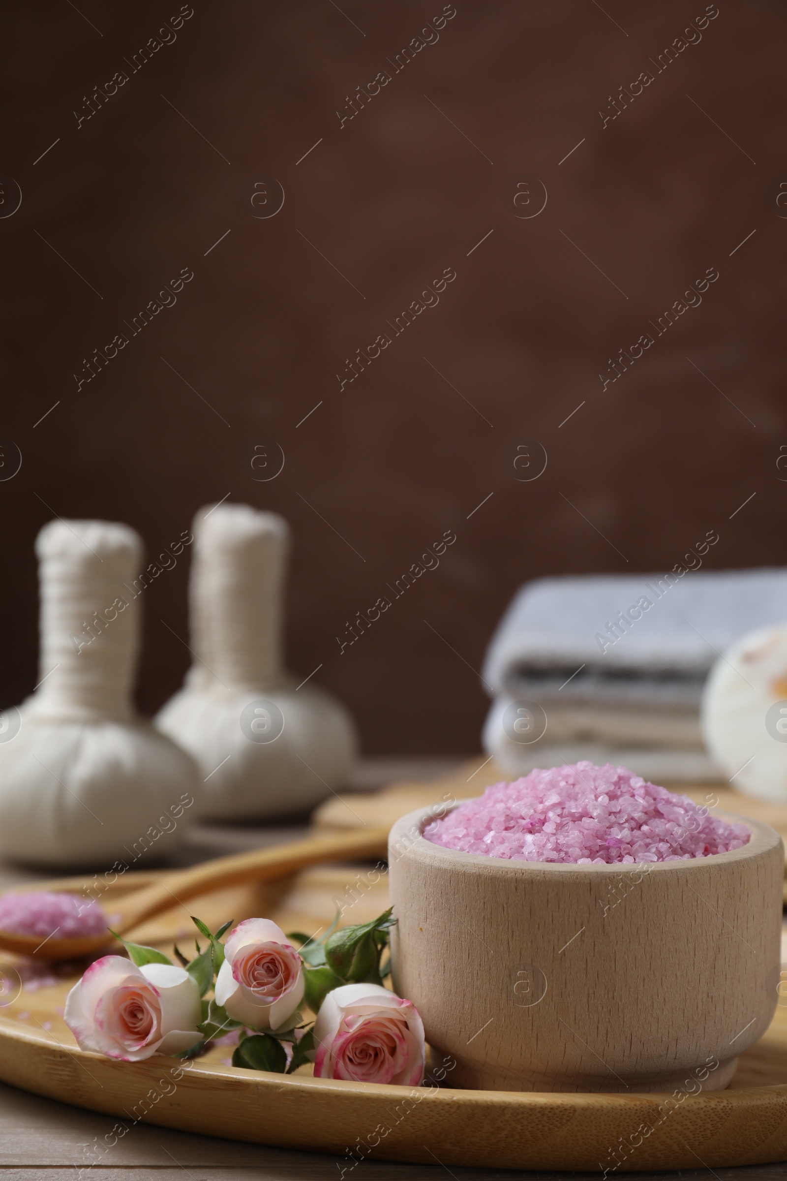Photo of Bowl of pink sea salt and roses on wooden table. Space for text