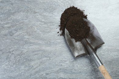 Photo of Metal shovel with fertile soil on grey textured surface, top view. Space for text