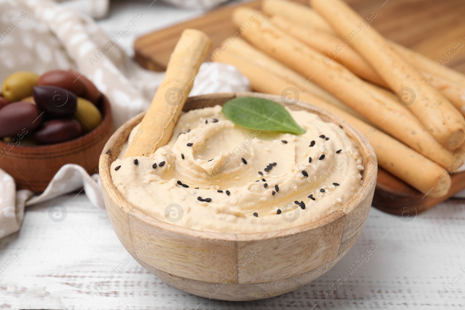 Photo of Delicious hummus with grissini stick on white wooden table, closeup