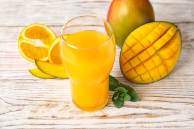 Glass with fresh mango juice and tasty fruits on wooden table