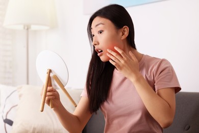 Suffering from allergy. Young woman with mirror checking her face in living room