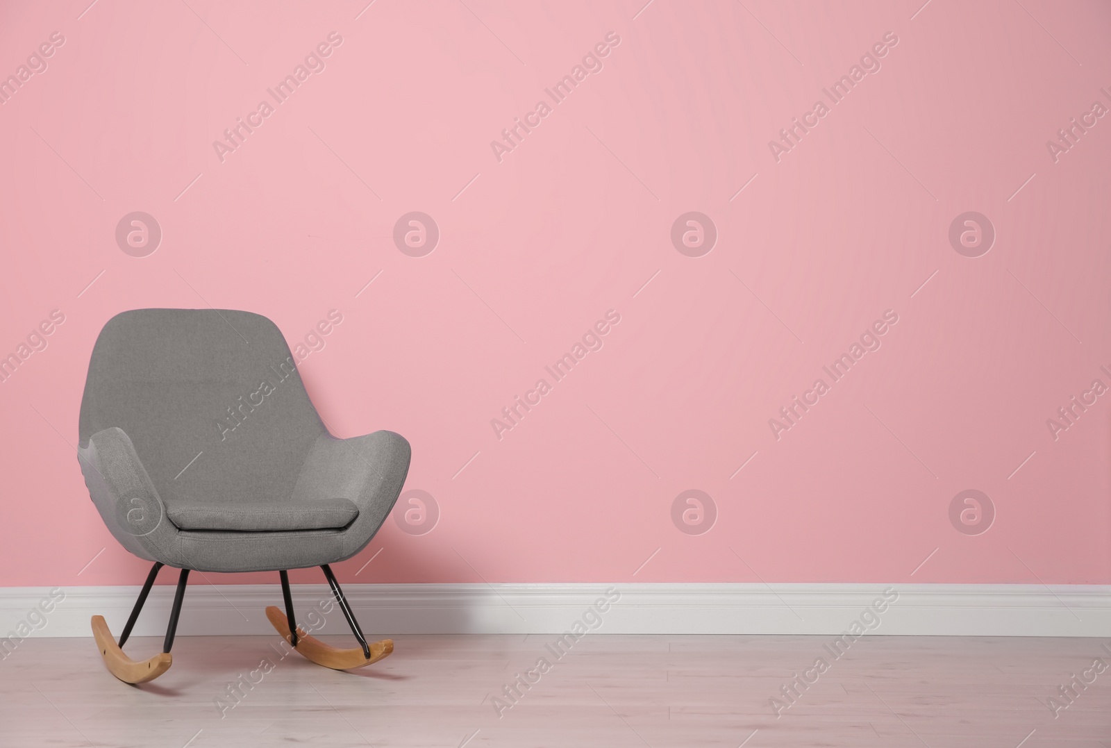 Photo of Comfortable rocking chair near color wall. Modern interior element