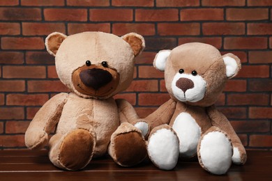 Cute teddy bears on wooden table near brick wall
