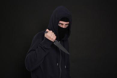 Man in mask with knife on black background. Dangerous criminal