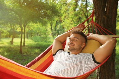 Young man resting in comfortable hammock at green garden