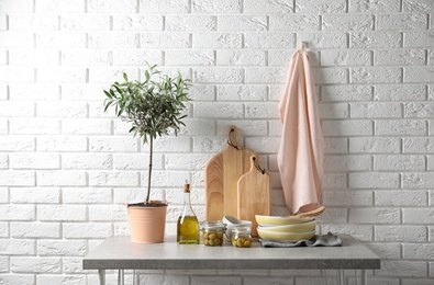 Fresh oil, olives and kitchen utensils on table near brick wall