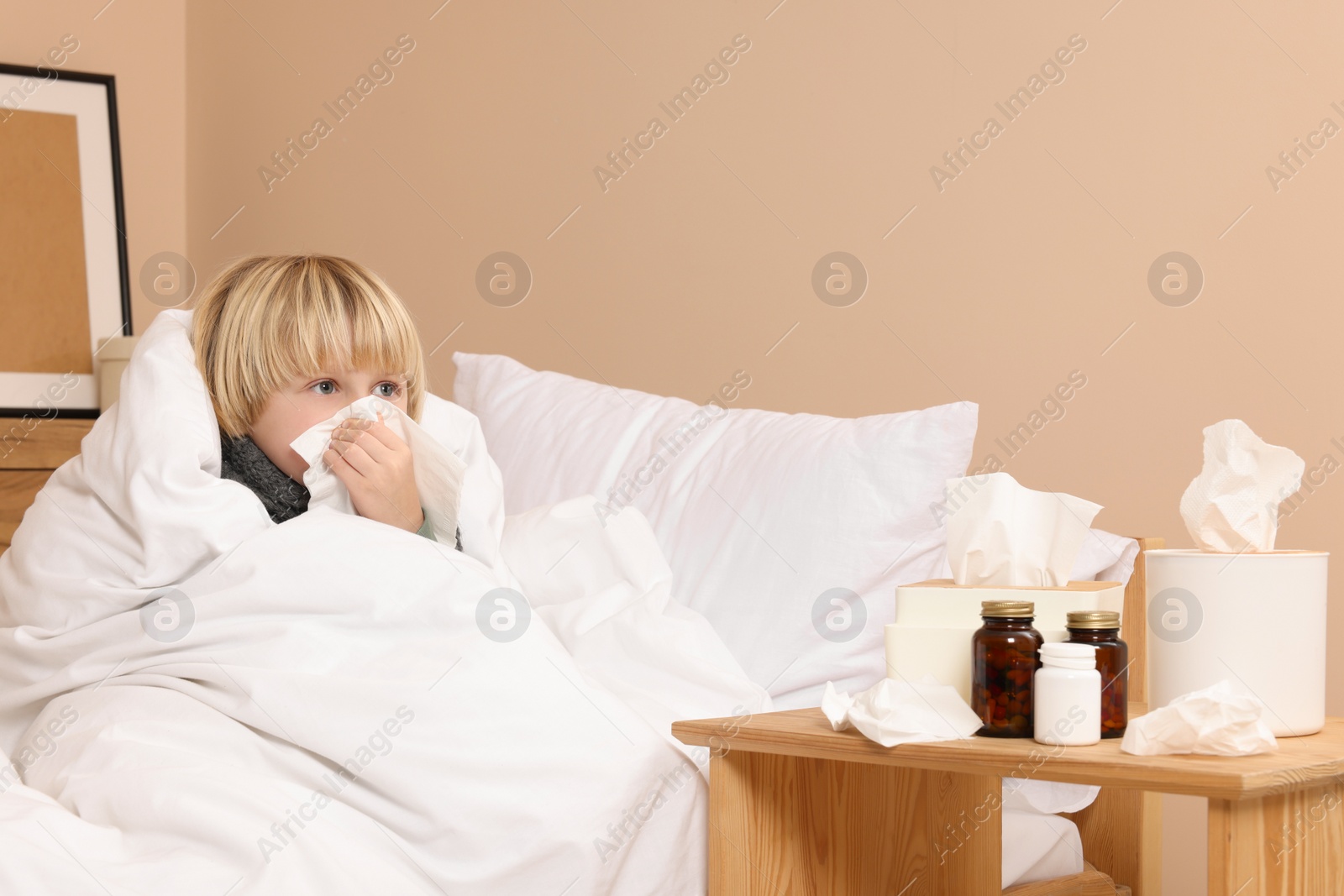 Photo of Boy blowing nose in tissue in bed at home. Cold symptoms