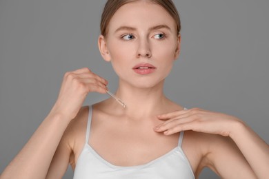 Photo of Beautiful young woman applying essential oil onto collarbone on grey background