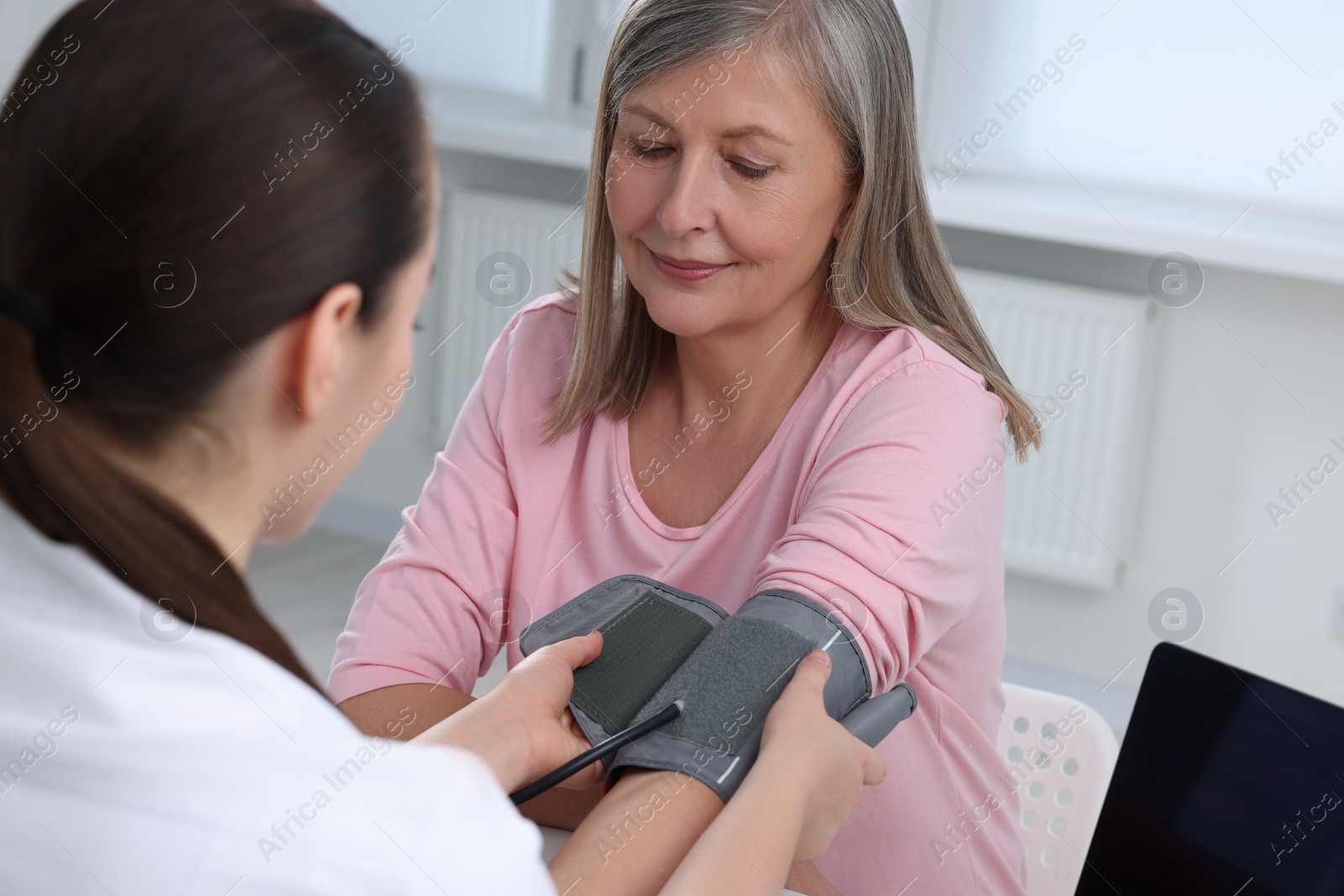 Photo of Doctor measuring blood pressure of woman at table indoors