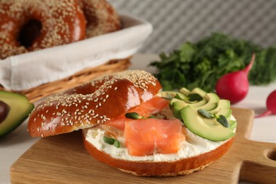 Delicious bagel with cream cheese, salmon, avocado and microgreens on wooden board, closeup