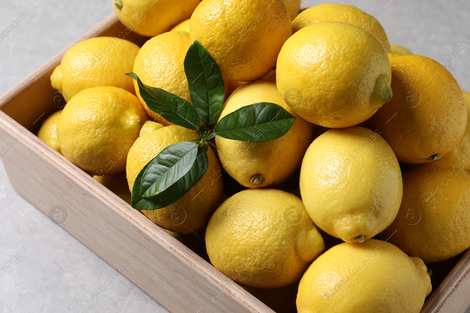 Photo of Fresh lemons in wooden crate on grey table, closeup