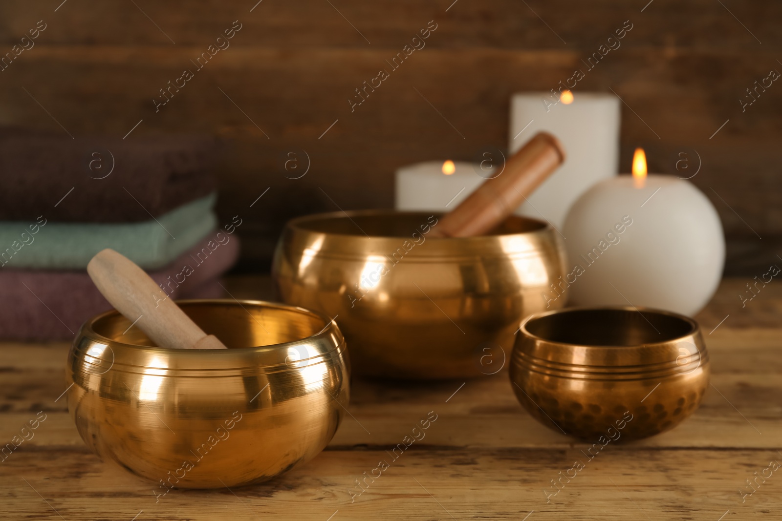 Photo of Golden singing bowls with mallets and burning candles on wooden table