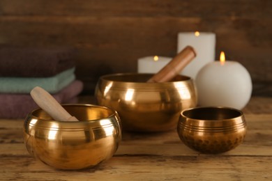 Photo of Golden singing bowls with mallets and burning candles on wooden table