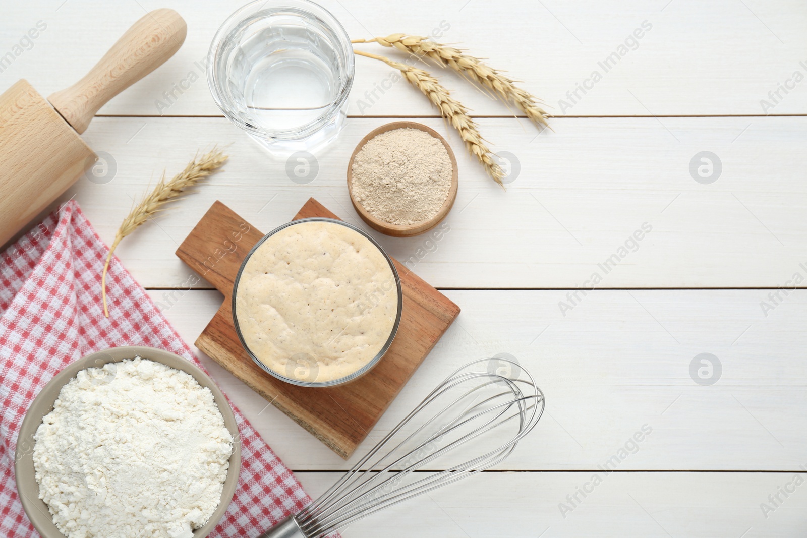 Photo of Leaven, flour, water, rolling pin, whisk and ears of wheat on white wooden table, flat lay. Space for text