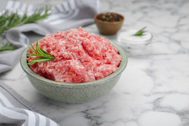 Bowl of raw fresh minced meat with rosemary on white marble table, closeup. Space for text