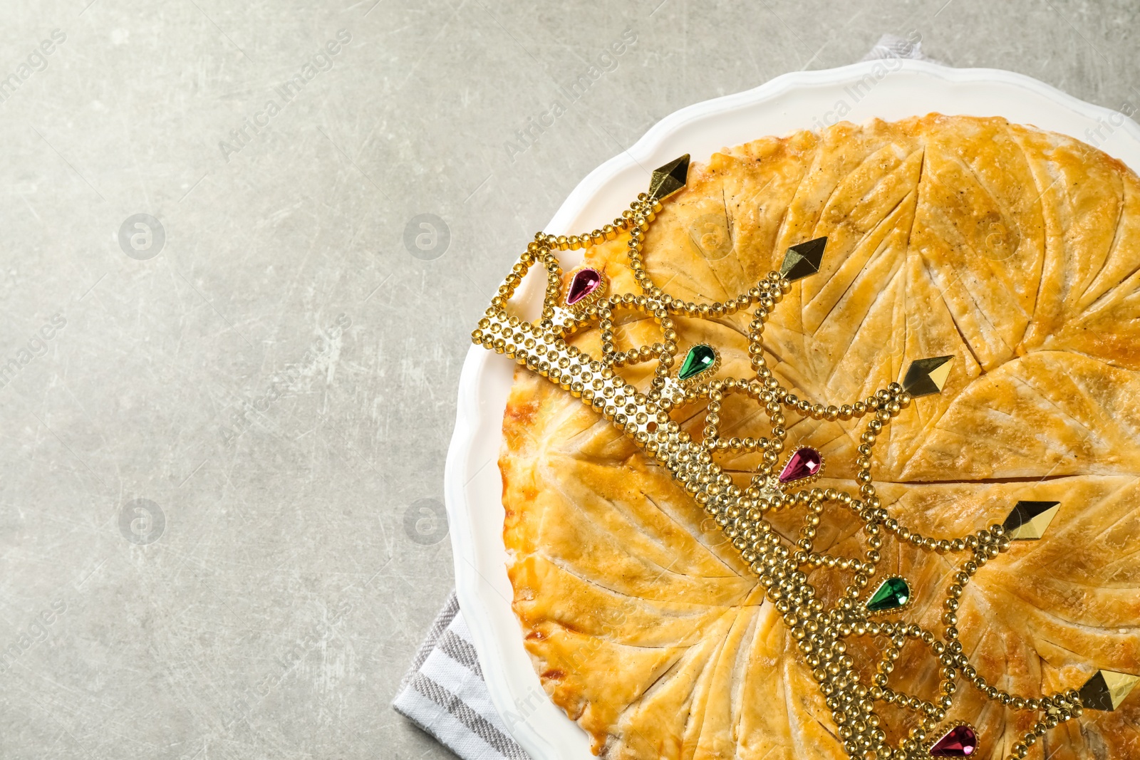 Photo of Traditional galette des Rois with decorative crown on light grey table, flat lay. Space for text