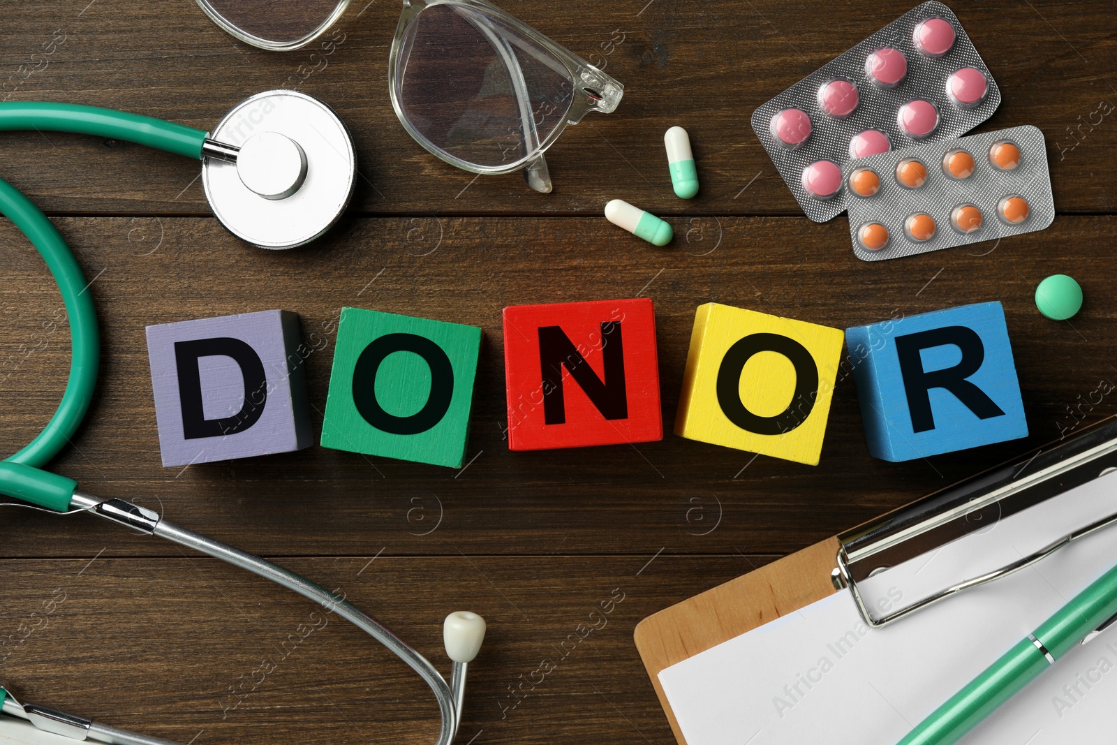 Photo of Word Donor made of colorful cubes, pills, clipboard and stethoscope on wooden table, flat lay