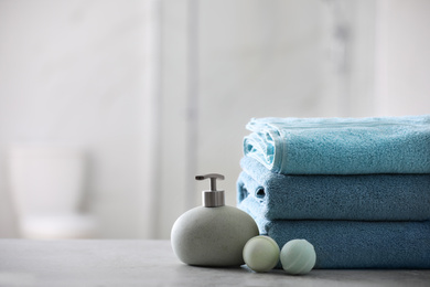 Photo of Stack of fresh towels, soap dispenser and bath bombs on table indoors. Space for text