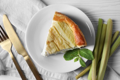 Photo of Piece of freshly baked rhubarb pie, stalks and cutlery on white wooden table, flat lay