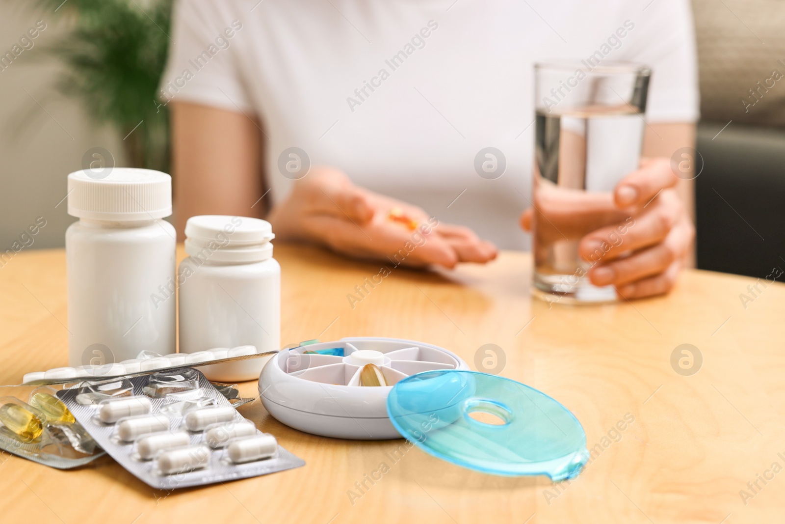 Photo of Woman with pills, organizer and glass of water at light wooden table, selective focus