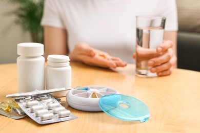 Woman with pills, organizer and glass of water at light wooden table, selective focus