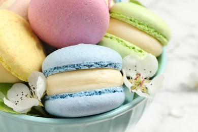 Photo of Delicious colorful macarons and flowers in bowl on table, closeup