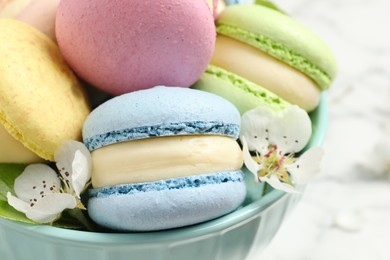 Delicious colorful macarons and flowers in bowl on table, closeup