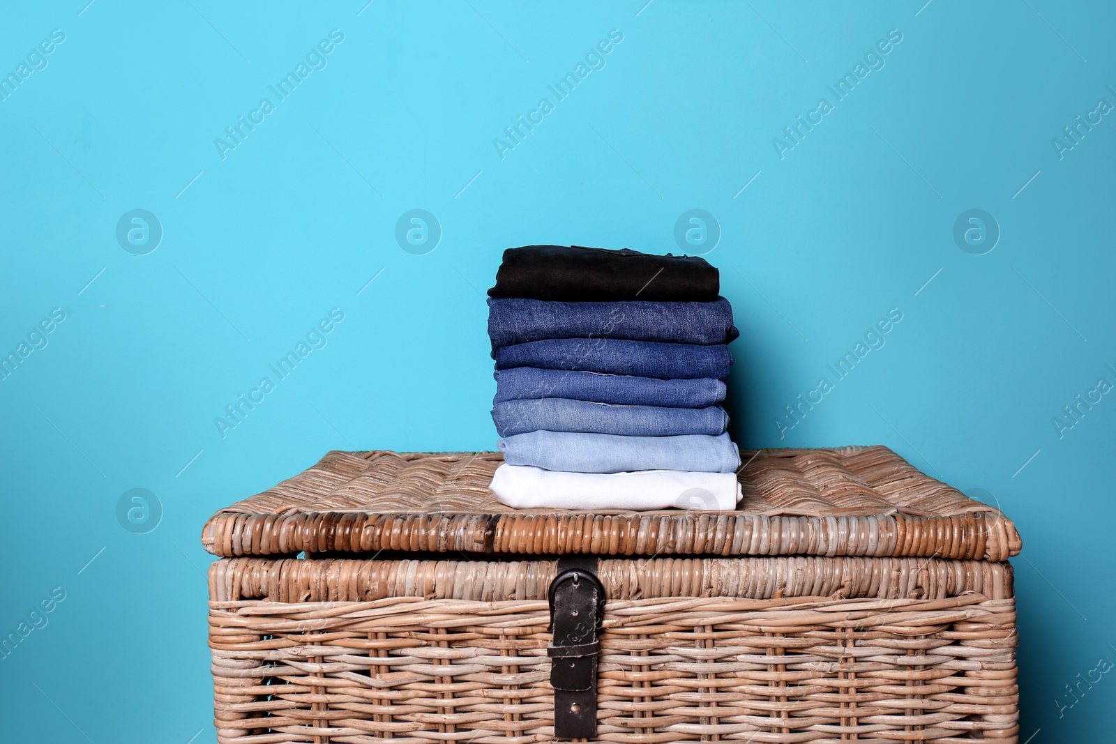 Photo of Stack of different jeans on basket against color wall