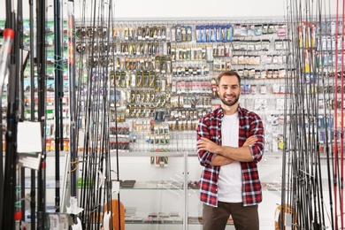 Photo of Man standing near showcase with fishing equipment in sports shop. Space for text