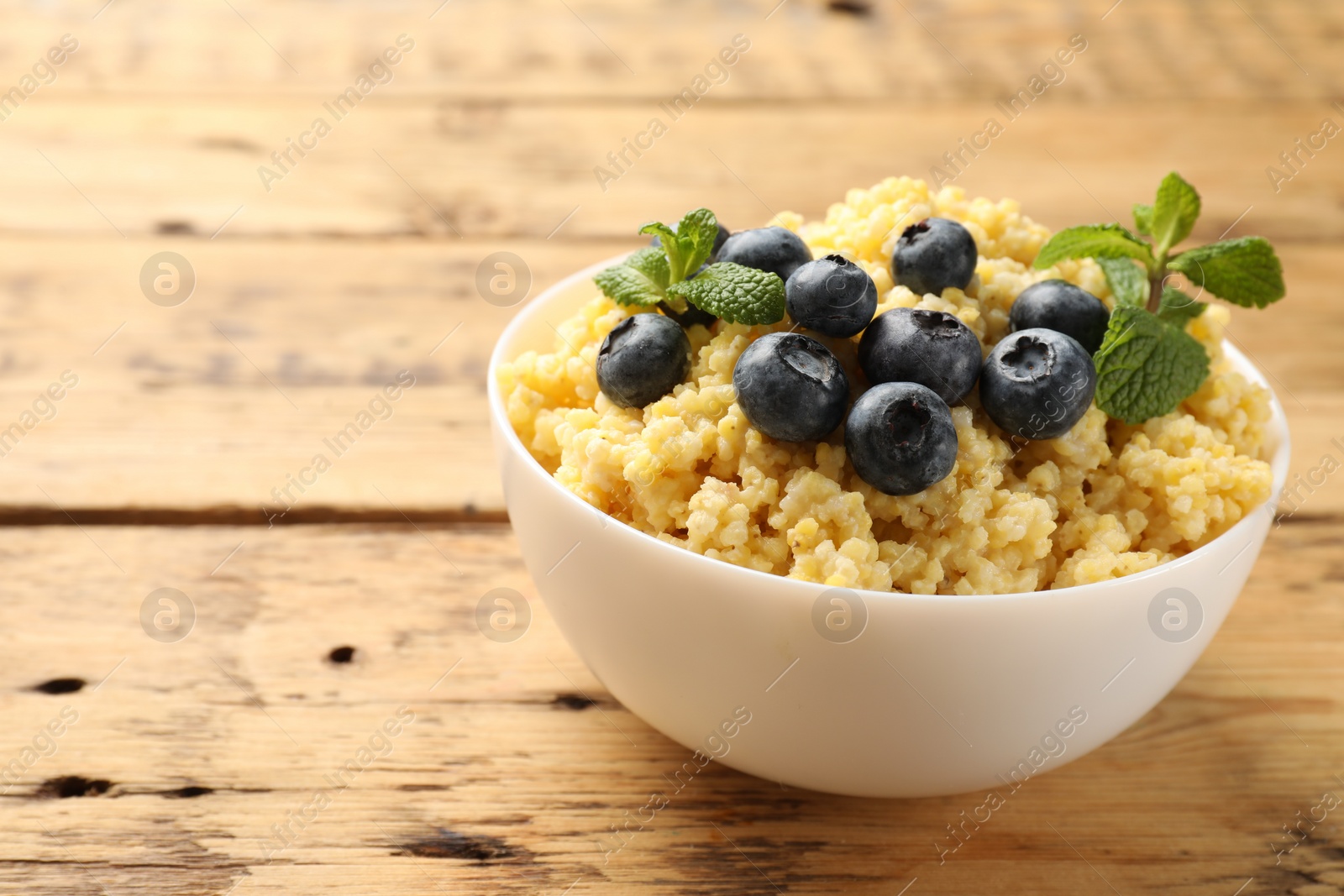 Photo of Tasty millet porridge with blueberries and mint in bowl on wooden table, closeup. Space for text