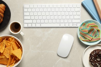 Photo of Bad eating habits at workplace. White keyboard and different snacks on light grey marble table, flat lay