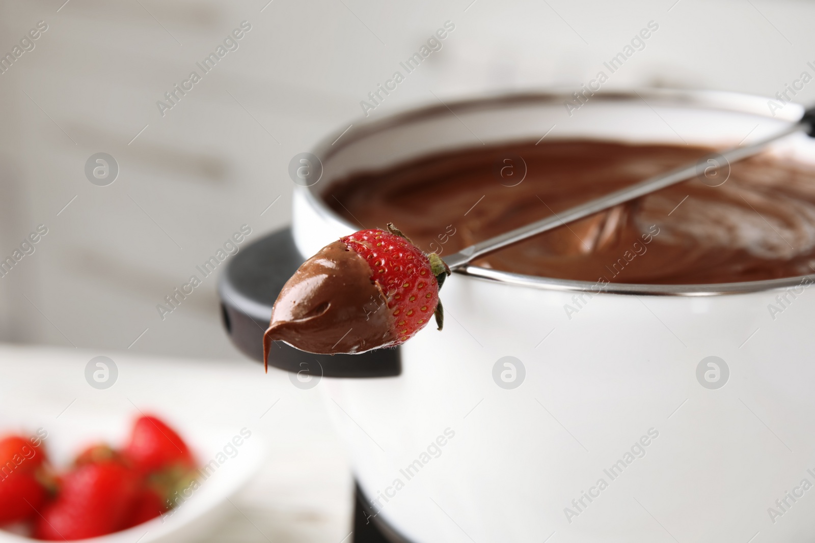 Photo of Pot with chocolate fondue and dipped strawberry on table, closeup