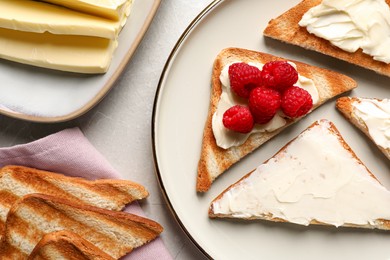 Photo of Tasty toasts with butter and raspberries on light grey table, flat lay