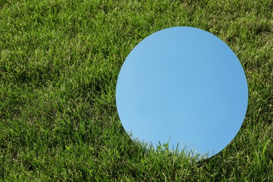 Photo of Round mirror on grass reflecting sky. Space for text