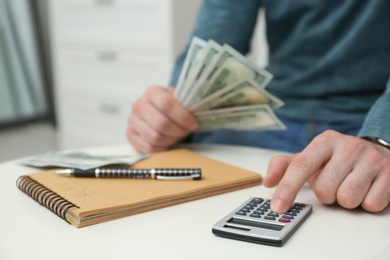 Photo of Man with money, notebook and calculator at table indoors, closeup