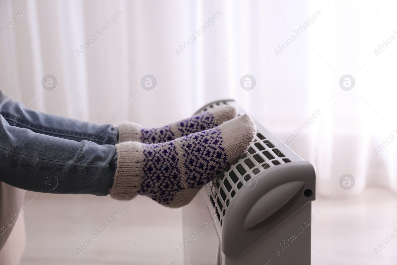 Photo of Child warming feet on electric heater at home, closeup