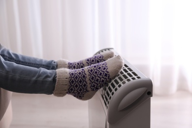 Child warming feet on electric heater at home, closeup