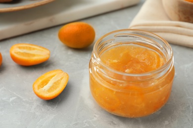 Photo of Delicious kumquat jam and fresh fruits on light grey marble table