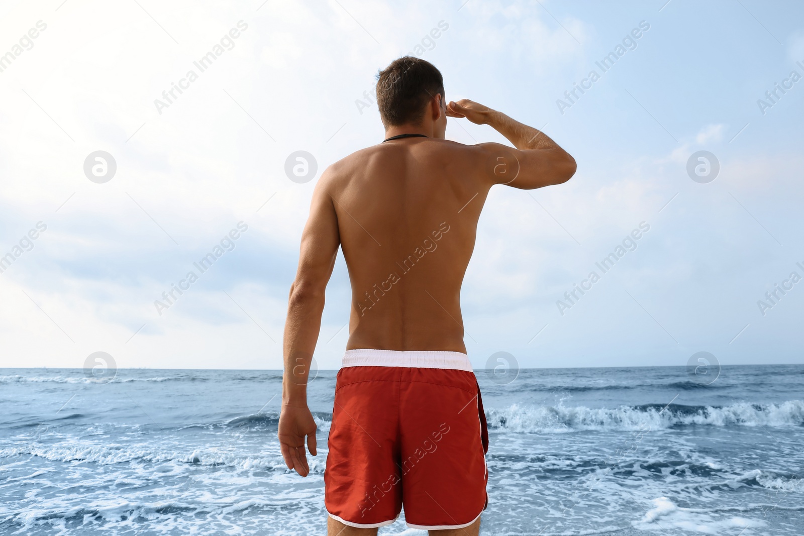 Photo of Handsome lifeguard near sea on summer day, back view