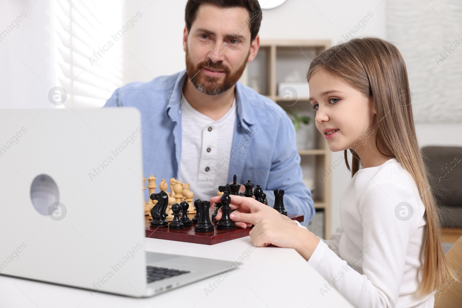 Photo of Father teaching his daughter to play chess following online lesson at home