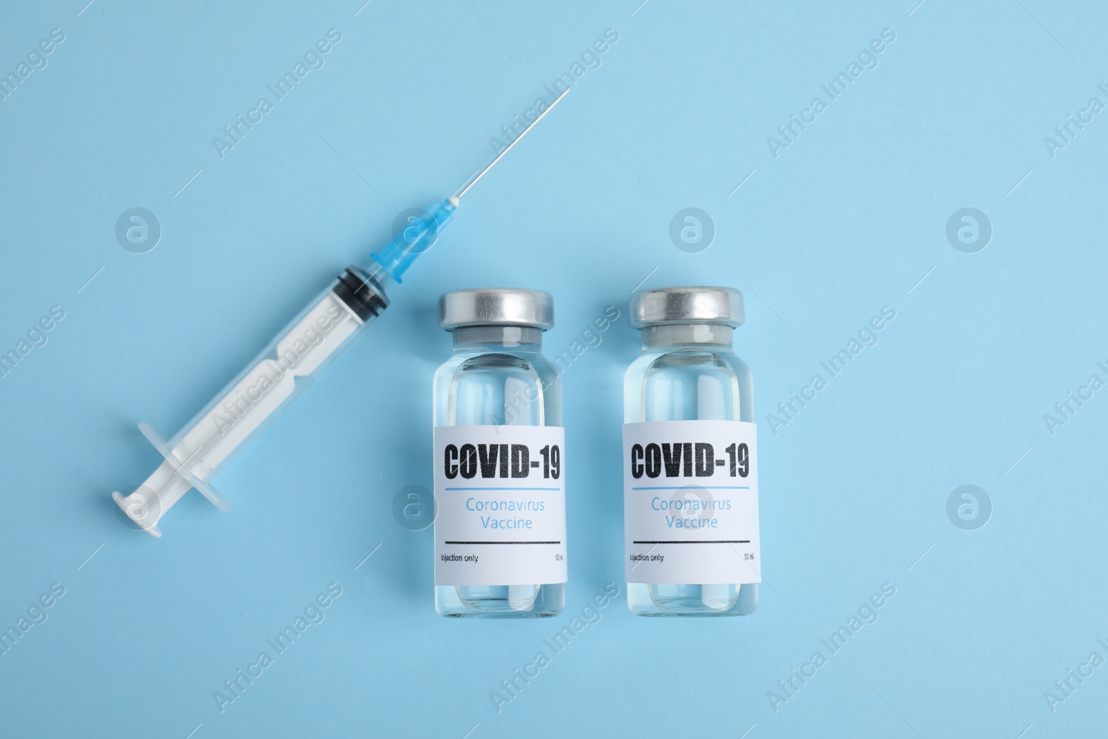 Photo of Vials with coronavirus vaccine and syringe on light blue background, flat lay