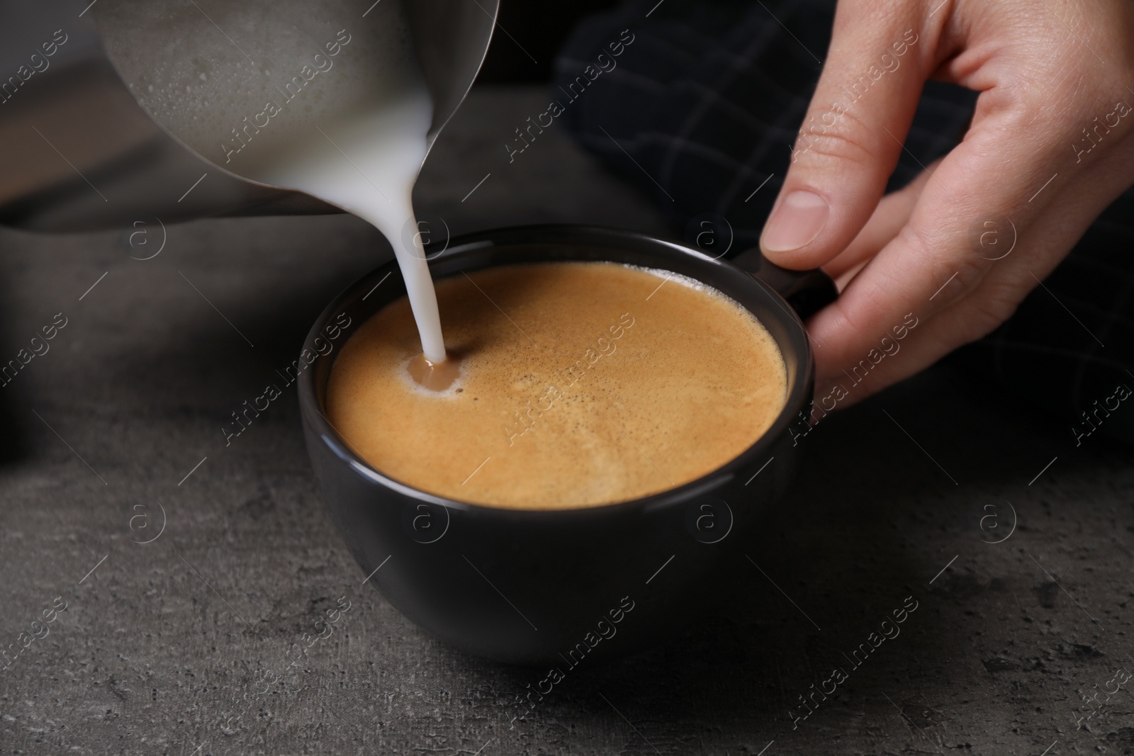 Photo of Woman pouring milk into cup of coffee at grey table, closeup