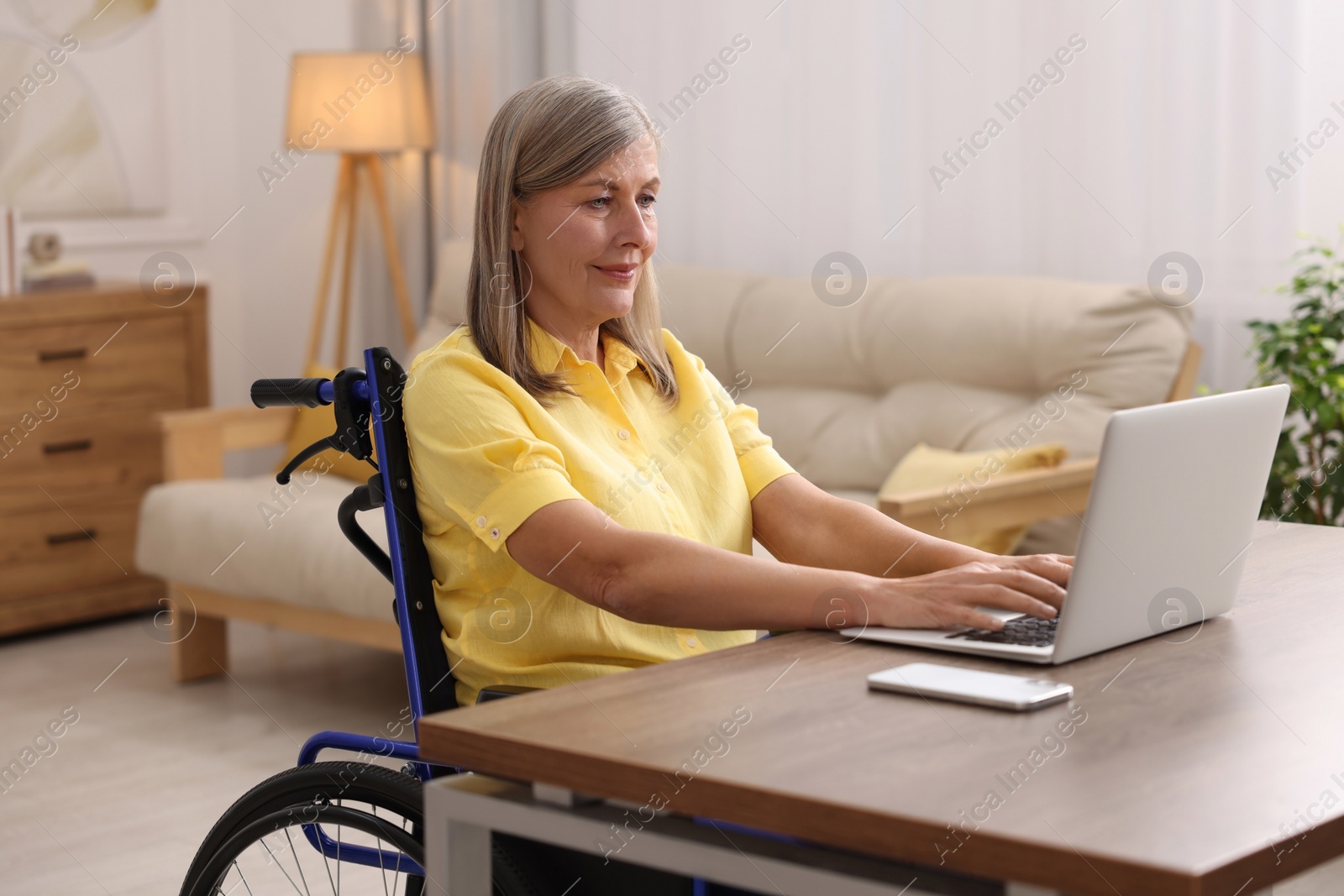 Photo of Woman in wheelchair using laptop at table in home office