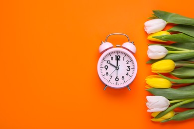 Pink alarm clock and beautiful tulips on orange background, flat lay with space for text. Spring time