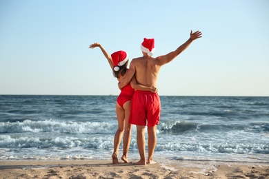 Lovely couple with Santa hats together on beach, back view. Christmas vacation