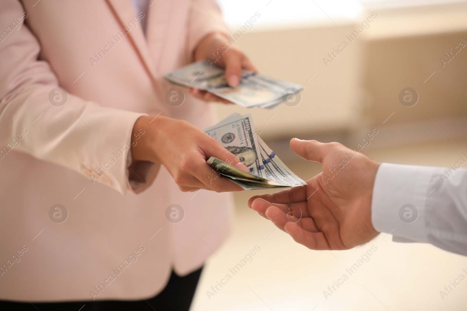 Photo of Businesswoman giving dollar bills to man on blurred background, closeup