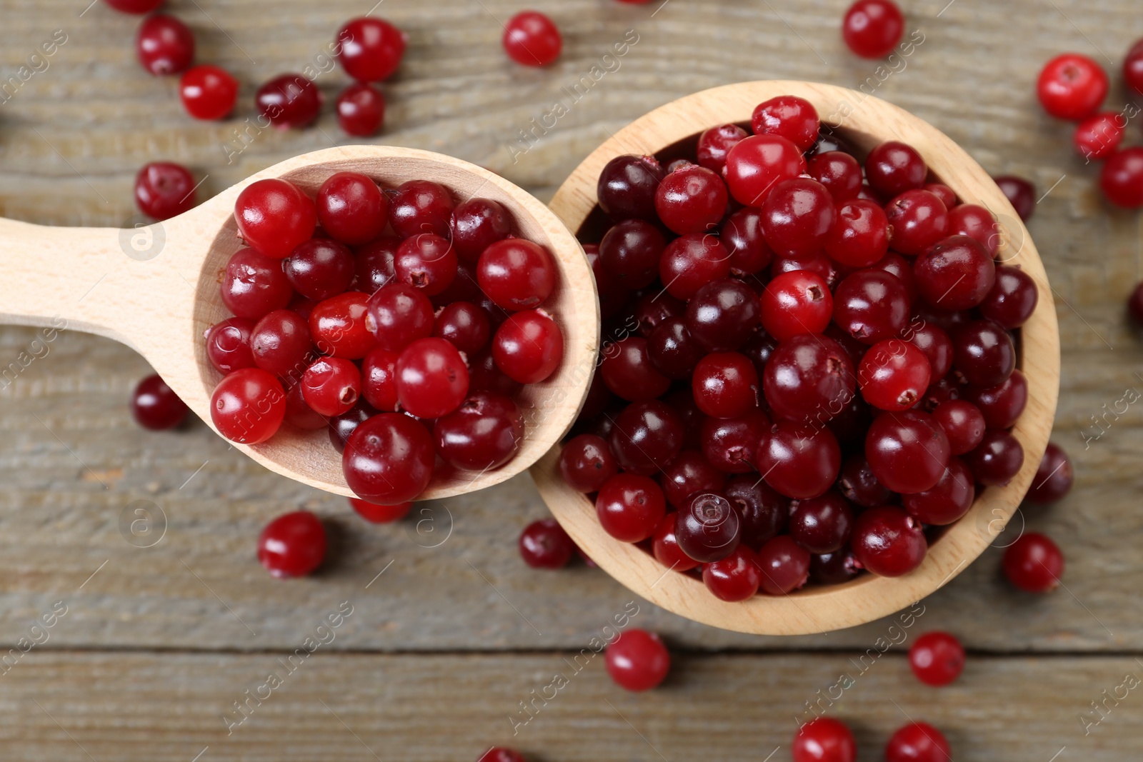 Photo of Fresh ripe cranberries in bowl and spoon on wooden table, top view