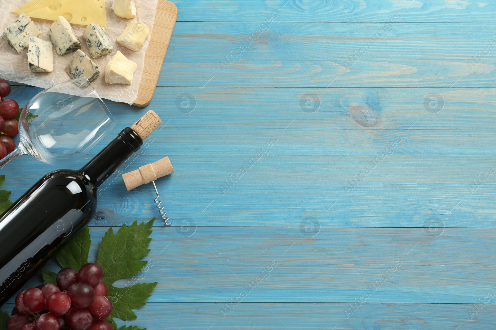 Photo of Tasty red wine and snacks on light blue wooden table, flat lay. Space for text