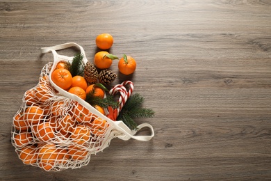 Flat lay Christmas composition with fresh tangerines in mesh bag on wooden table. Space for text