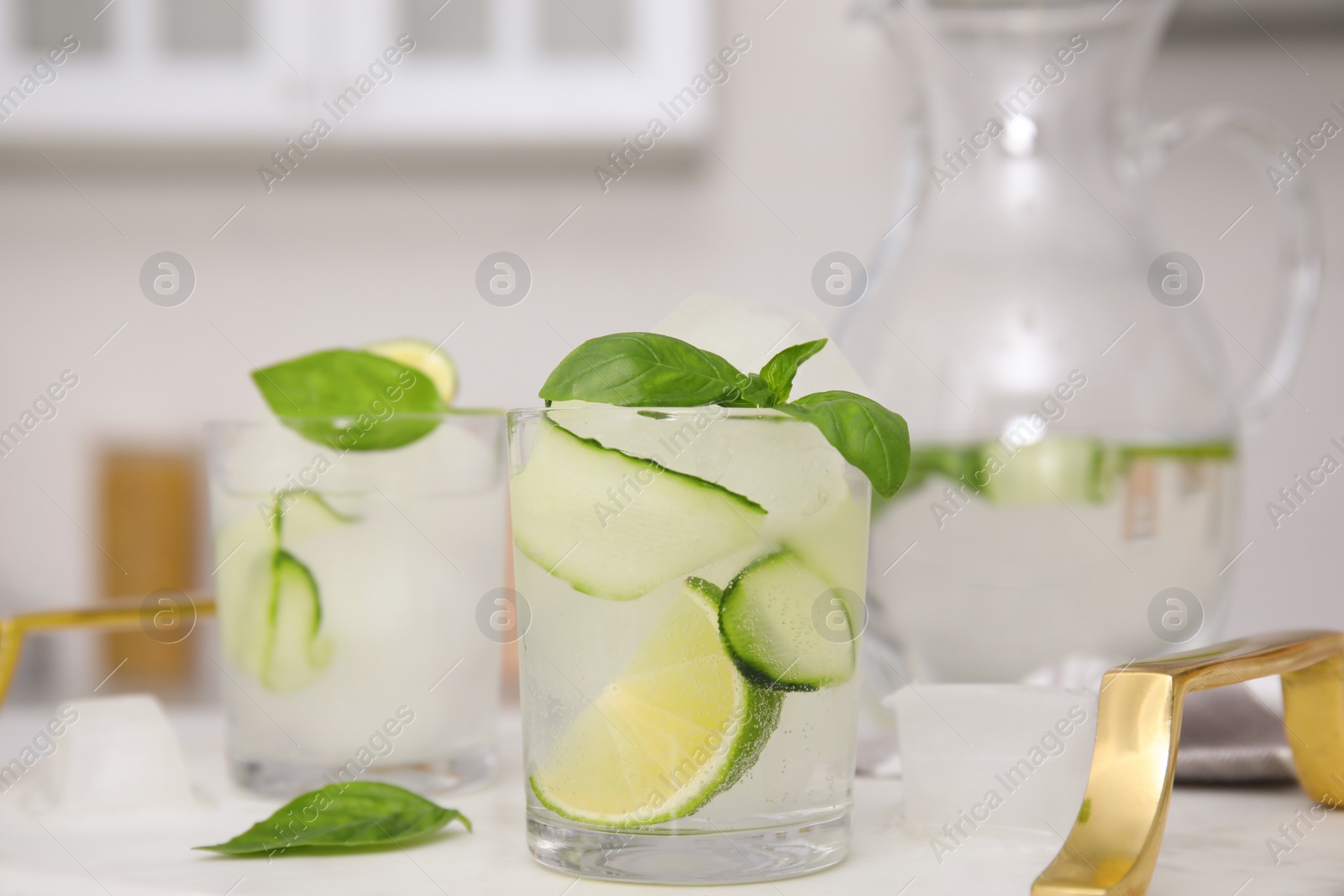 Photo of Tasty fresh cucumber water with sliced lime and basil on white table indoors
